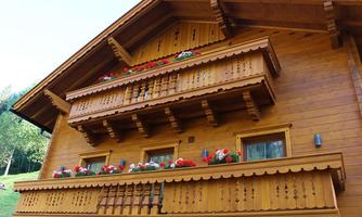 A traditional wooden house with a decorative balcony and colorful flower boxes. The green surroundings create a cozy atmosphere.