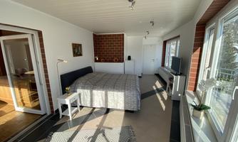 A modern bedroom with a large bed and plenty of natural light. The walls are bright, and there is a cozy atmosphere.