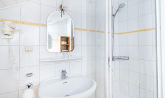 A modern bathroom with a shower, a sink, and a mirror. The walls are tiled and kept in light colors.