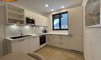 A modern kitchen with white cabinets and a large window overlooking a mountain landscape. The amenities include a stove, a sink, and a refrigerator.