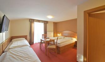 A spacious hotel room with two beds, a table, and a television. The room has large windows and a warm, welcoming color tone.
