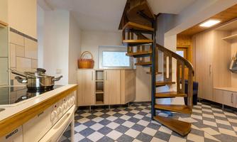 A bright kitchen with a modern spiral staircase. The floor is designed with checkerboard tiles in black and white.