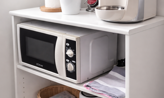 A modern kitchenette with a microwave, a kettle, and other kitchen utensils. Dish towels and a basket are also visible on the shelf.
