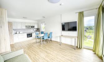A modern, bright apartment with an open kitchen and a dining area. Large windows offer a view of nature and plenty of natural light.