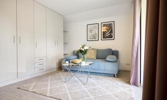 A cozy room with a blue sofa and a table. Pictures hang on the wall, and there is a rug on the floor.