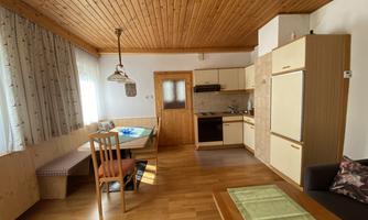 A cozy kitchen with wooden floors and wooden ceilings. It includes a dining table, chairs, and modern kitchen elements.