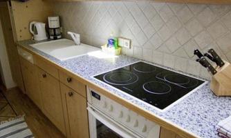 A modern kitchen with wooden cabinets and a light countertop. On the counter are a coffee machine, a kettle, and a cooking hob.