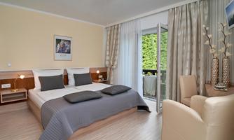 A modern bedroom with two beds and a cozy armchair. The room has large windows that lead to a balcony.