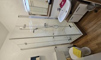 A modern bathroom with a shower cabin, a sink, and a toilet. The room has a bright and inviting atmosphere.