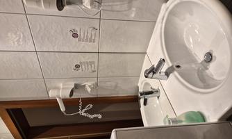 A bathroom with two sinks and a hairdryer on the wall. The walls are tiled and there are some indications of hygiene.