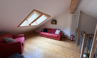 A cozy living room with red sofas and wooden flooring. Large windows provide plenty of daylight.