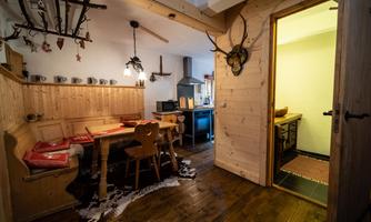 A cozy room with wooden furniture and a small dining area. The walls are clad in wood, and there is an open kitchenette.