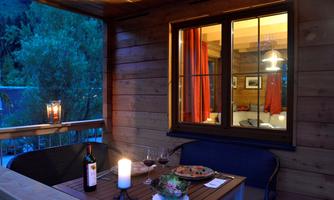 A cozy balcony with a table on which wine and a dish are placed. Through the window, one can see the warm interior.