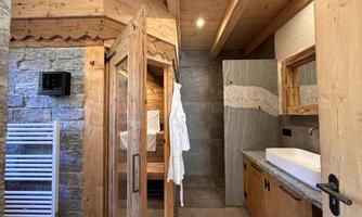 A modern bathroom with warm wooden details and a sauna. The decor is simple and inviting, featuring a large sink and a towel warmer.