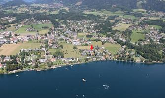 Aerial view of a picturesque lake, surrounded by green meadows and small towns. In the foreground, boats are visible on the water.