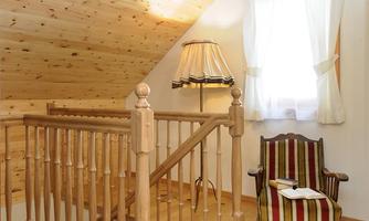 A cozy room with wooden paneling and stairs. A chair with striped upholstery is next to a window with curtains.
