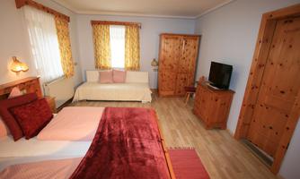 A cozy bedroom with two beds and a sofa bed. There are wooden wardrobes and large windows with curtains.