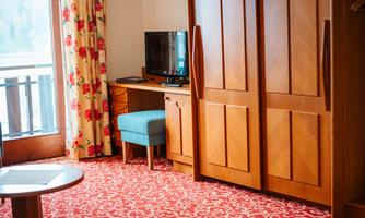 A cozy hotel room with red carpet and wooden furniture. There is a television, a table, and a wardrobe.