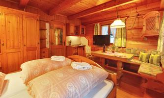 A cozy wooden room with a double bed and a seating area. The room is well-lit and invites relaxation.