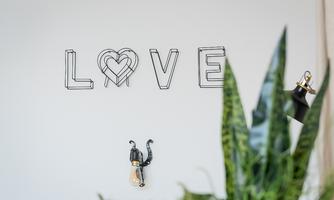 A wall with stylized letters that form the word "LOVE" can be seen. In the foreground, there are green plants and a decorative lamp.