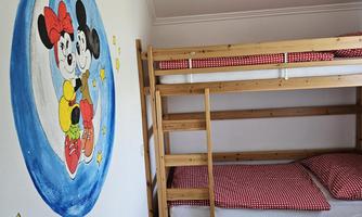 A children's room with a wooden bunk bed and a colorful mural of Mickey Mouse. The bedding is red checkered.