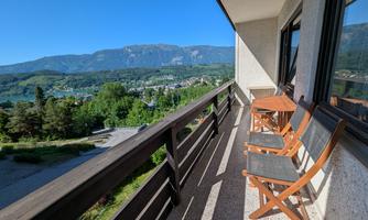 A sunny balcony with two chairs and a table. In the background, mountains and a beautiful view of the valley can be seen.