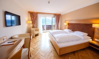 A modern hotel room with two beds and a balcony. The room is bright and tastefully furnished, with a television and a table.