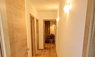 A bright hallway with wooden flooring and modern doors. Soft light sources are installed on the walls.