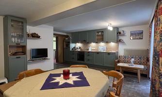 A cozy dining kitchen with a large wooden table and modern furniture. The walls are decorated with colorful curtains, and the kitchen is well-equipped.