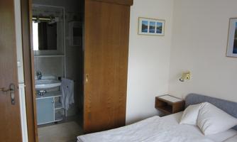 A simple room with a single bed and an adjoining bathroom. The walls are light and there are some decorative pictures.