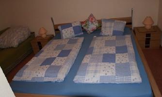 A bedroom with a double bed and blue checkered bedspreads. Next to the bed are two nightstands with lamps.