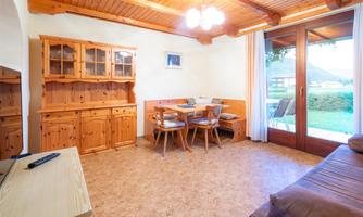 An inviting living space with wooden furniture and a table for four people. Large windows offer a view of the greenery.