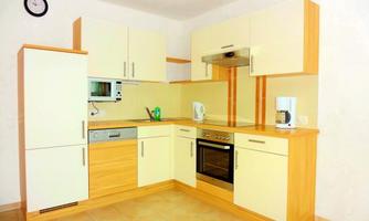 A modern kitchen with bright furniture and a well-equipped cooking area. It includes a stove, a microwave, and various electric appliances.