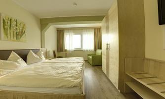 A modern hotel room with two beds and a cozy seating area. Large windows provide plenty of daylight.