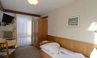 A simple bedroom with a bed, a table, and a television. There is a window with curtains and a wooden dresser.