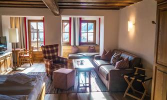 A cozy room with a wooden ceiling and large windows. There is a living room with a sofa, an armchair, and a table.