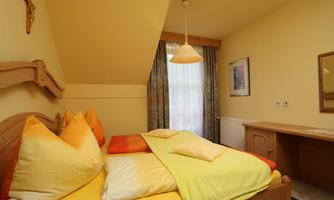 A cozy bedroom with a large bed and colorful cushions. The room has light walls and a window with curtains.