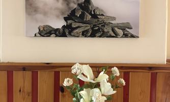 An image of mountains shrouded in clouds is displayed on the wall. Below, there is a vase with fresh flowers on a table.