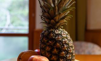 A fresh fruit bowl with pineapple, apples, bananas, and strawberries. The background shows a window with natural light.
