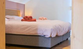 A cozy bedroom with a large bed and soft blankets. Freshly folded towels are placed on the bed.