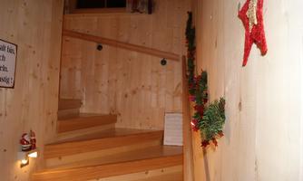 A cozy wooden staircase leads up into a warm, festive room. On the wall are Christmas decorations with lights and a small Santa Claus.