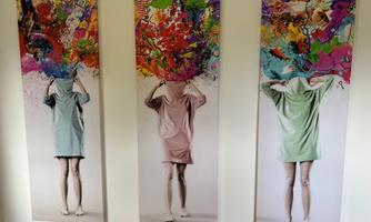 Three large artworks depict a person in a T-shirt, with their head covered. Above their head, colorful colors and shapes are bubbling.