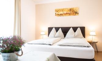 A cozy bedroom with a large double bed and two nightstands. A beautiful art print hangs on the wall, and a table with flowers is in the foreground.