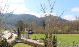 A green meadow with trees and a view of gentle hills. There is a path and some sculptures in the foreground.