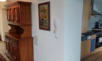An inviting hallway with a traditional wooden wardrobe and a piece of artwork on the wall. To the right, the open kitchen is visible.