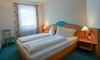 A bright bedroom with a double bed and white bedding. There is a chair and two bedside lamps.