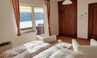 A bright bedroom with a double bed and two comfortable chairs. The window offers a view of the beautiful lake.