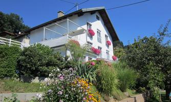 A charming house with blooming plants and a clear blue sky. The terrace is adorned with flowers and invites relaxation.