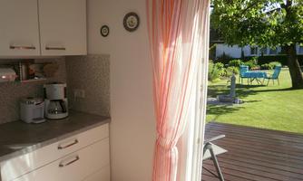 A bright kitchen with modern furniture and access to the garden. In the background, a cozy table and chairs can be seen outdoors.