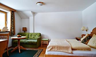 A cozy room with a double bed and a small seating area. The decor is simple and done in warm wooden tones.